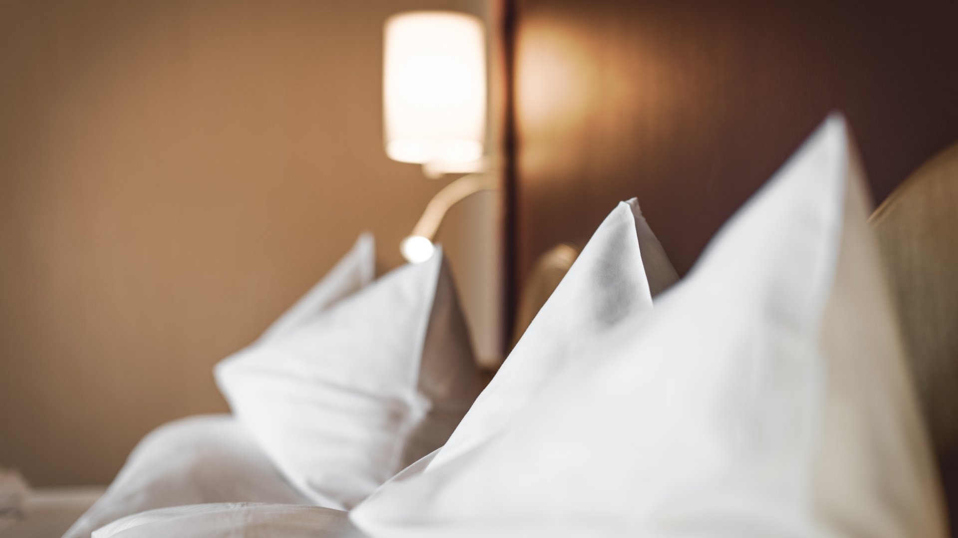 Nahaufnahme von weißen Kissen auf einem Bett mit Wandlampe im Hintergrund